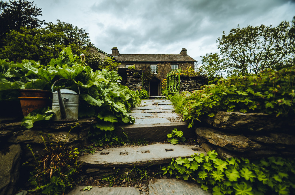 Quaint stone cottage with lush garden and stepping stone path under cloudy sky in countryside setting