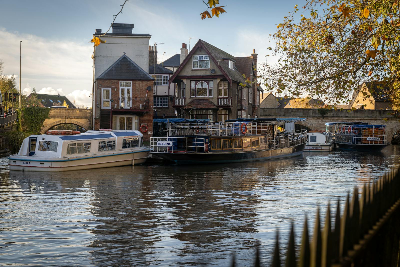 River view with boats and traditional buildings, surrounded by autumn trees, under a clear sky in a serene setting