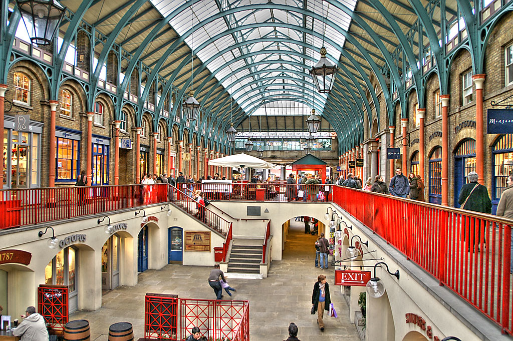 Bustling Covent Garden market interior with shops, vibrant red railings, and people shopping under a glass roof