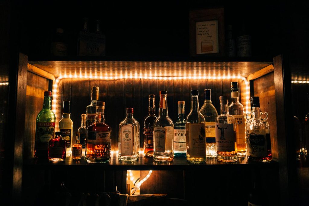 Illuminated shelf showcasing a variety of liquor bottles in a dimly lit bar setting with LED backlighting