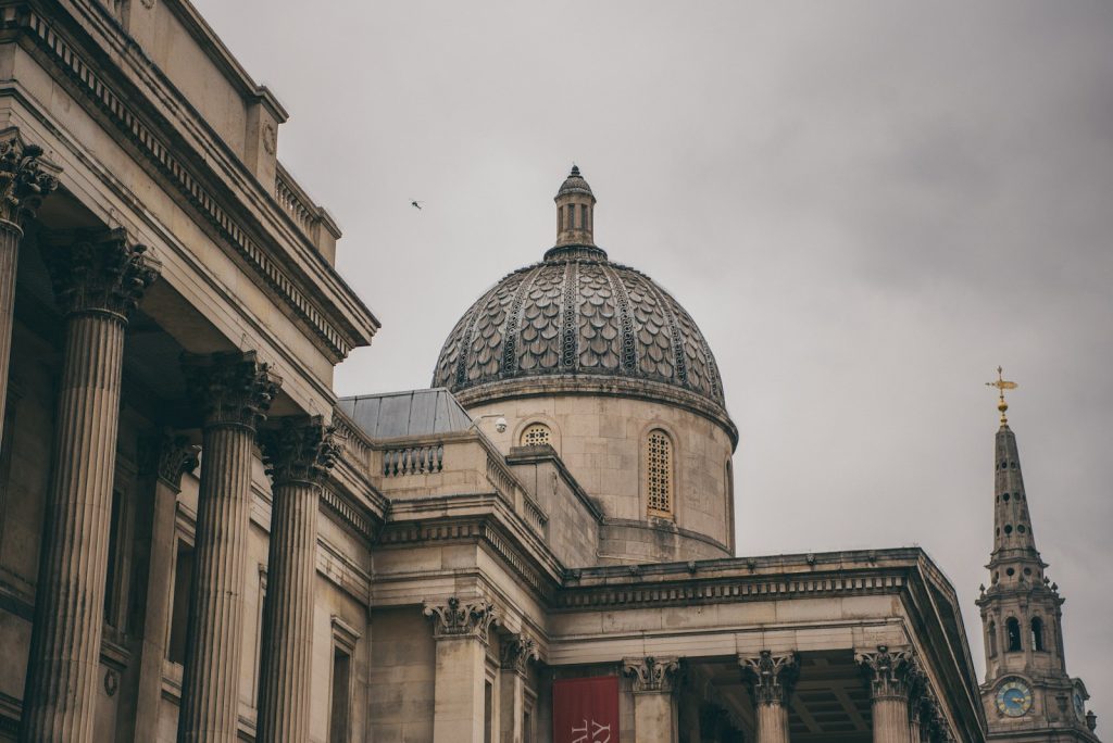 Historic London architecture featuring a classical dome and columns under a cloudy sky