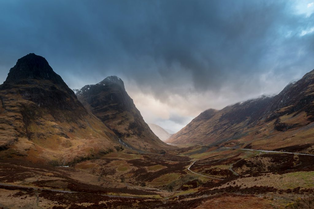Dramatic view of Glencoe Valley in Scotland with towering peaks and a cloudy sky