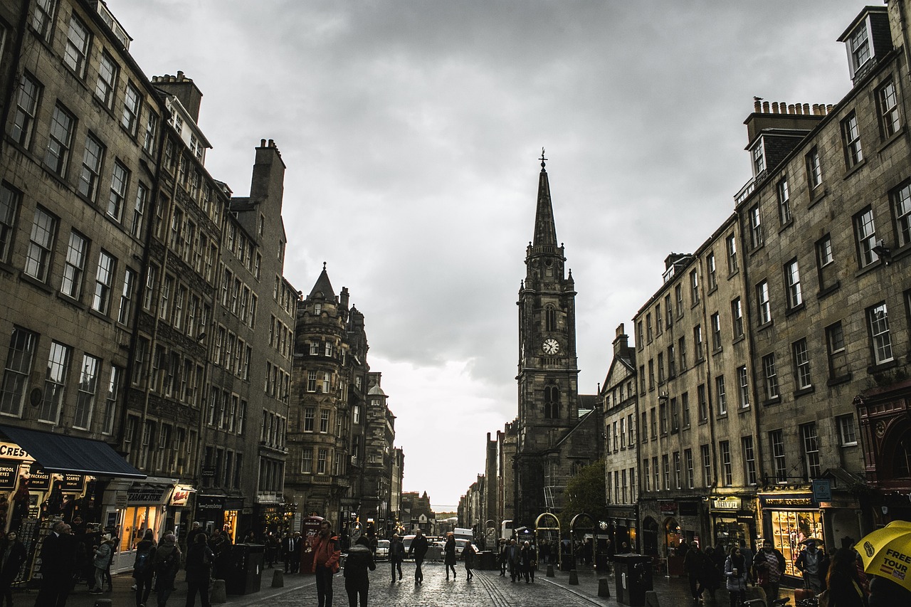 Historic Edinburgh street scene with iconic architecture and a cloudy sky, bustling with people and shops