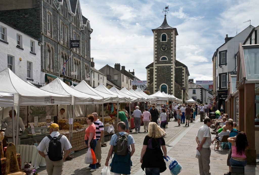 Bustling market scene in Keswick town centre with clock tower in the background and people shopping at stalls