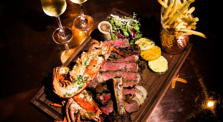 Gourmet surf and turf platter with steak, lobster, chips and wine on a luxurious dining table setting