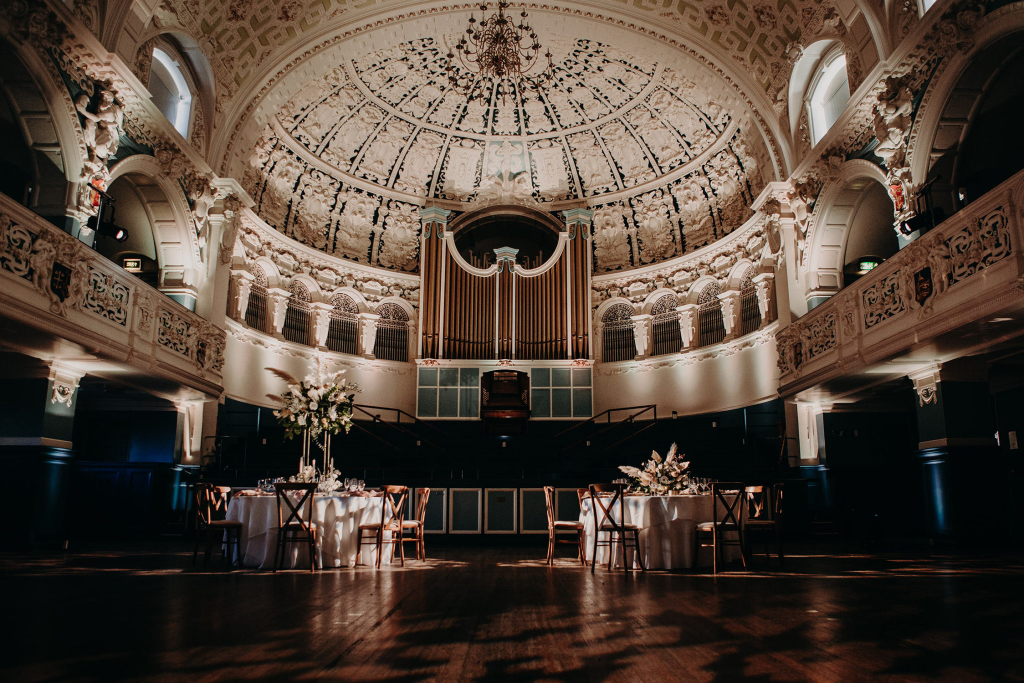 Elegant grand hall with ornate ceiling and set tables, perfect for weddings or events, featuring classical architecture
