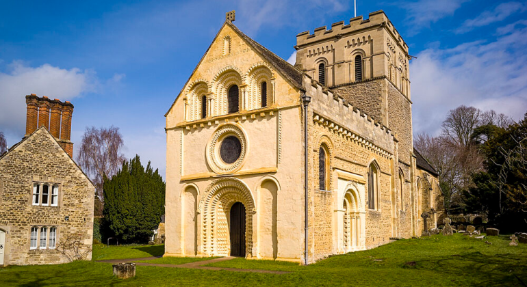 Historic English church with stone facade and trees under a bright blue sky