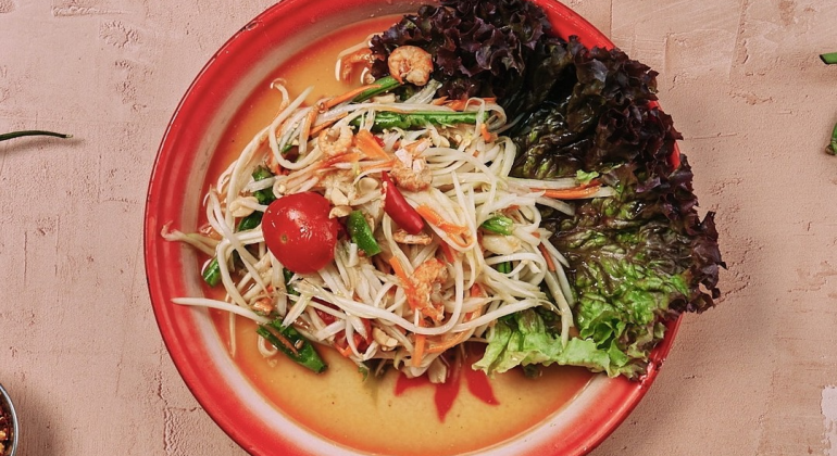 Thai papaya salad on a red plate, garnished with fresh lettuce and lime, showcasing vibrant, colourful ingredients