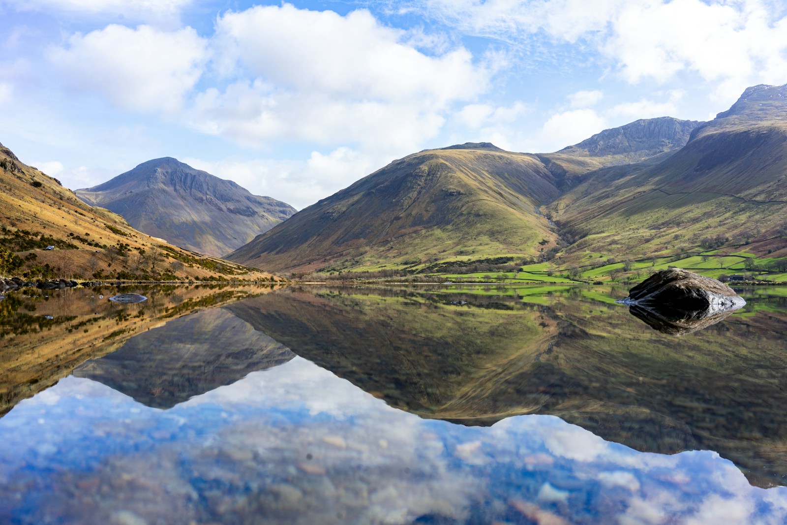 Mountain landscape reflected in calm lake with green hills and blue sky, peaceful natural scenery in the Lake District