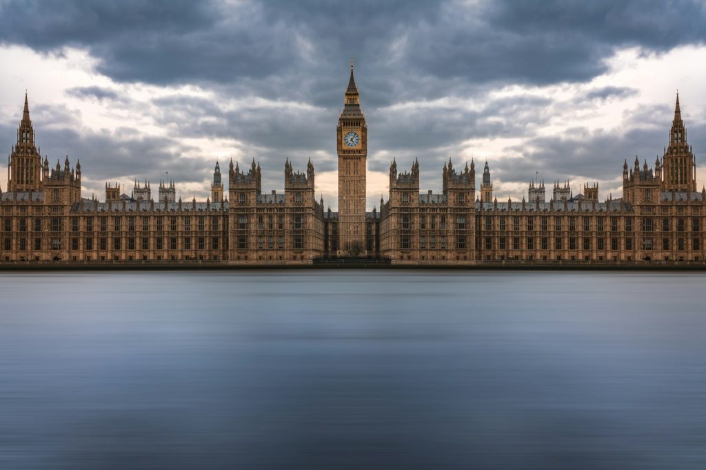 Palace of Westminster and Big Ben reflecting over River Thames under cloudy sky, London landmark architecture