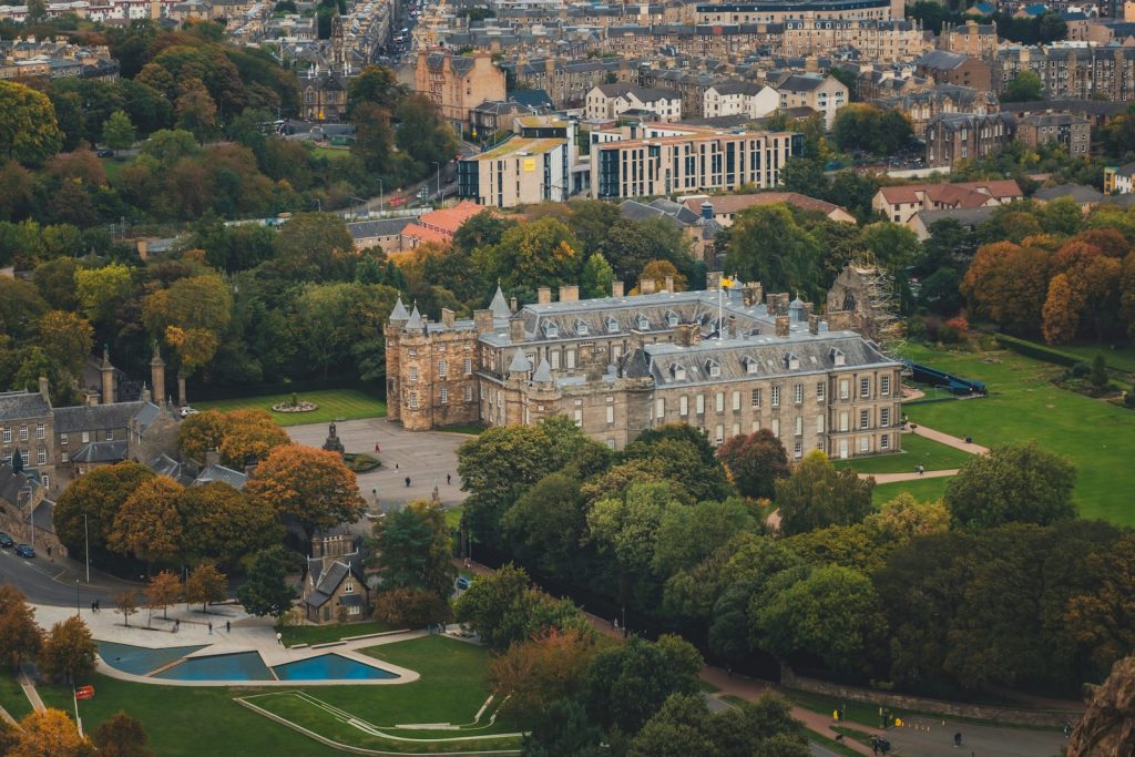 Aerial view of historic palace surrounded by lush gardens and cityscape in the background, vibrant autumn foliage visible