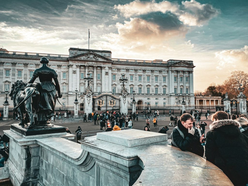 Crowd outside Buckingham Palace, London with dramatic sky and equestrian statue in foreground