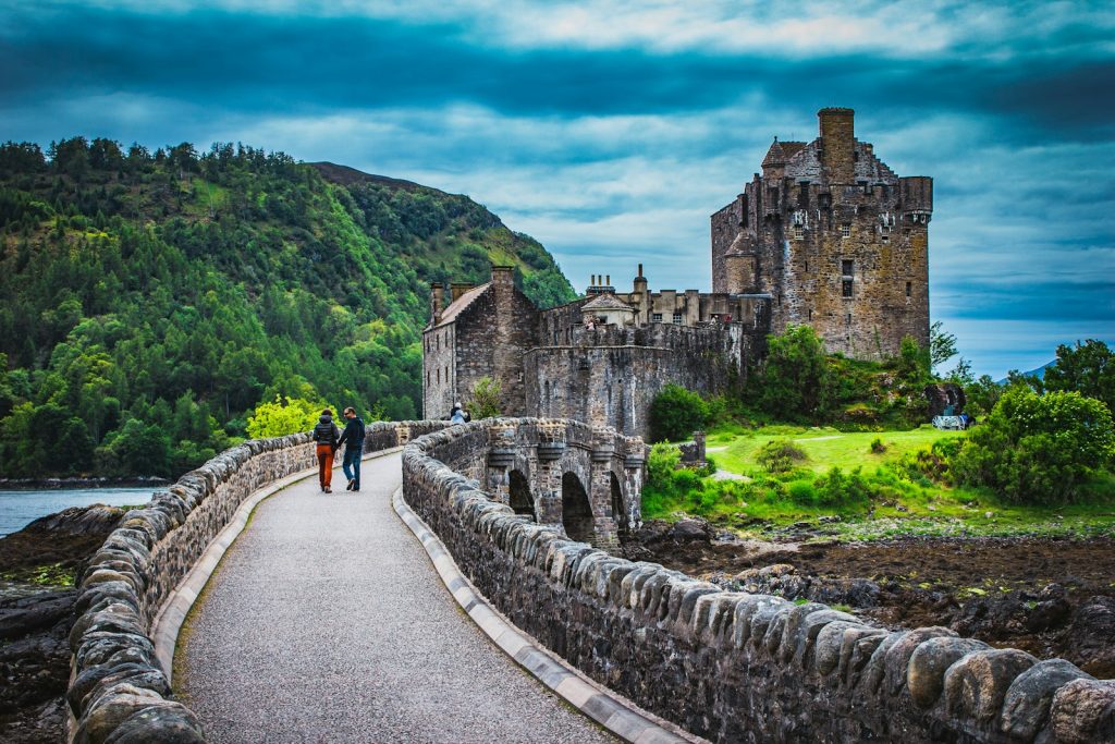 Scotland's Eilean Donan Castle with stone bridge, surrounded by lush greenery and dramatic sky
