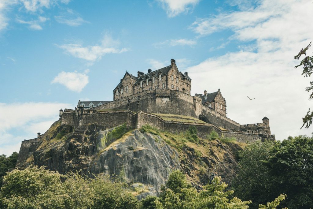 Historic castle on a rocky hill under a blue sky in the UK with lush greenery and a bird in flight