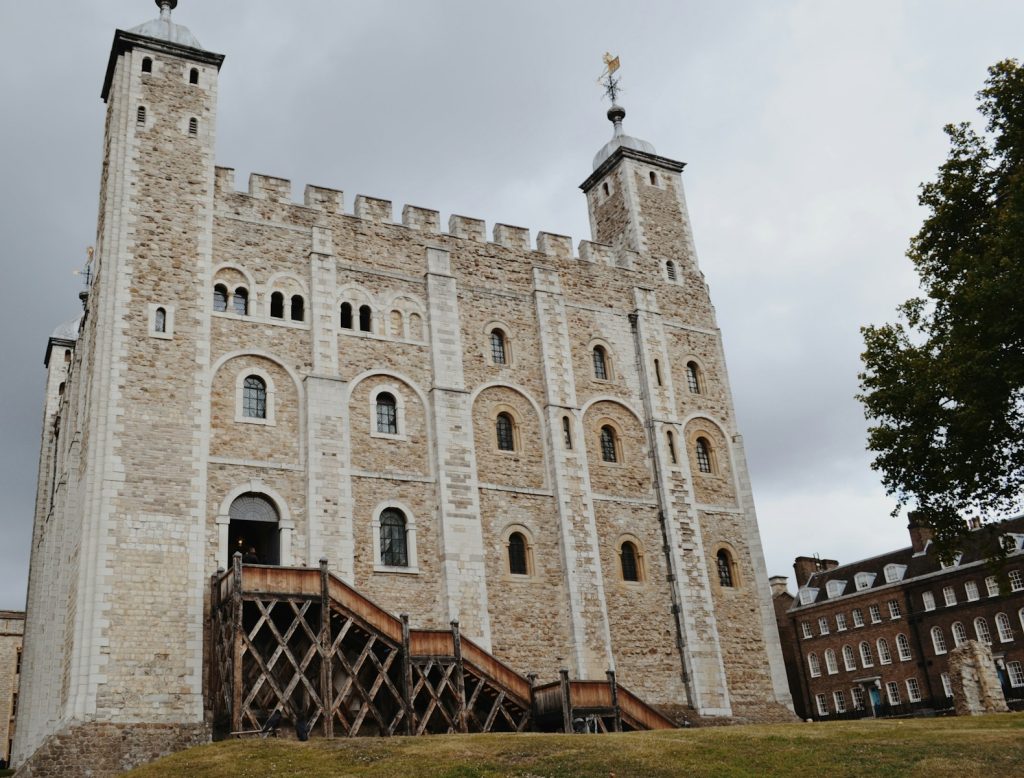 Historic Tower of London with cloudy sky, featuring medieval architecture and stone facade, surrounded by green lawn