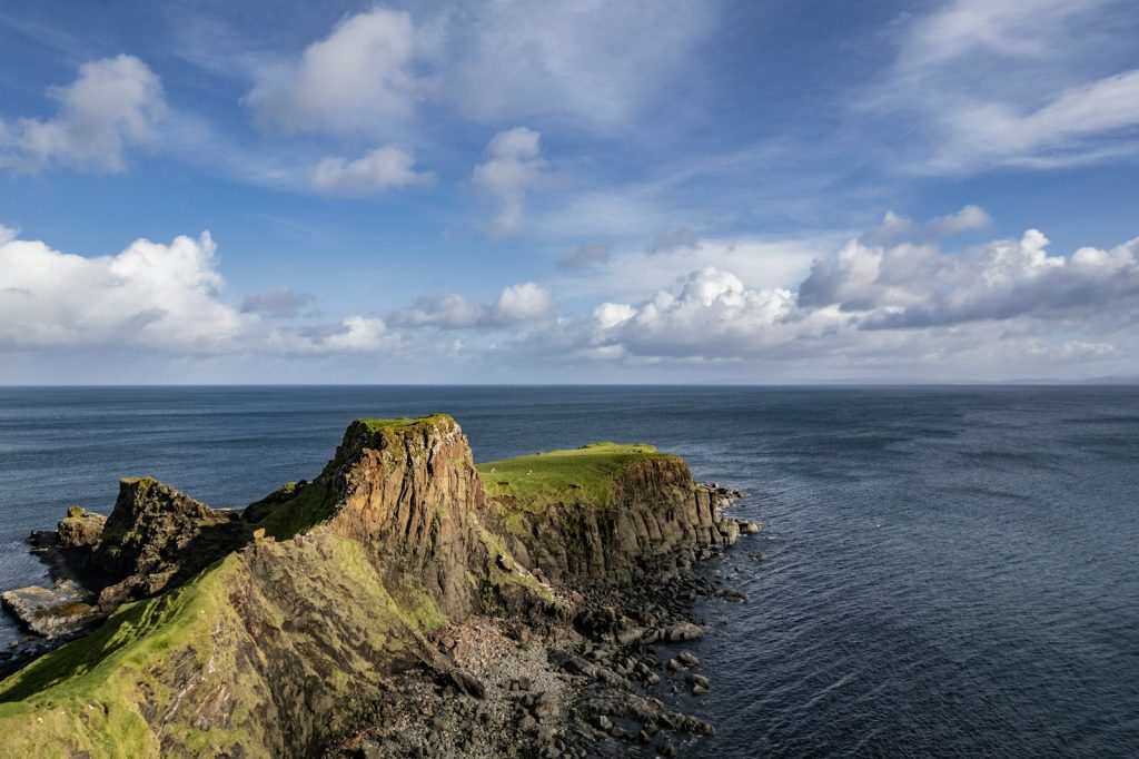 Rugged Scottish coastline with green cliffs overlooking the sea under a partly cloudy blue sky