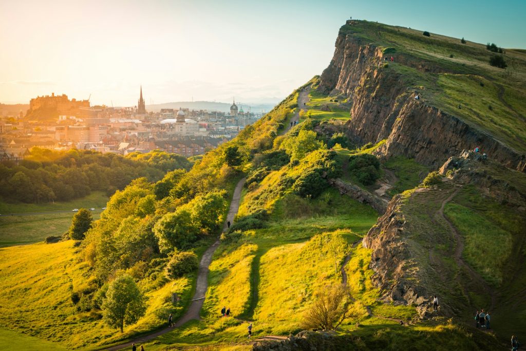 View of Arthur's Seat in Edinburgh during sunset with cityscape in the background, lush greenery and hiking trails