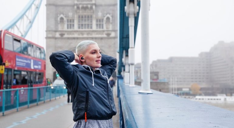 A woman stands on a bridge with Tower Bridge visible in the background, showcasing a scenic urban landscape