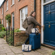 Person with luggage entering a brick house with a blue door in a quaint UK neighbourhood